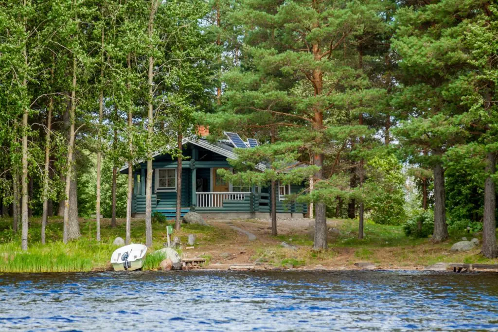 Wooden cabin overlooking a lake in Alberta surrounded by trees, representing seasonal cabins that are vulnerable to pest problems during the summer.